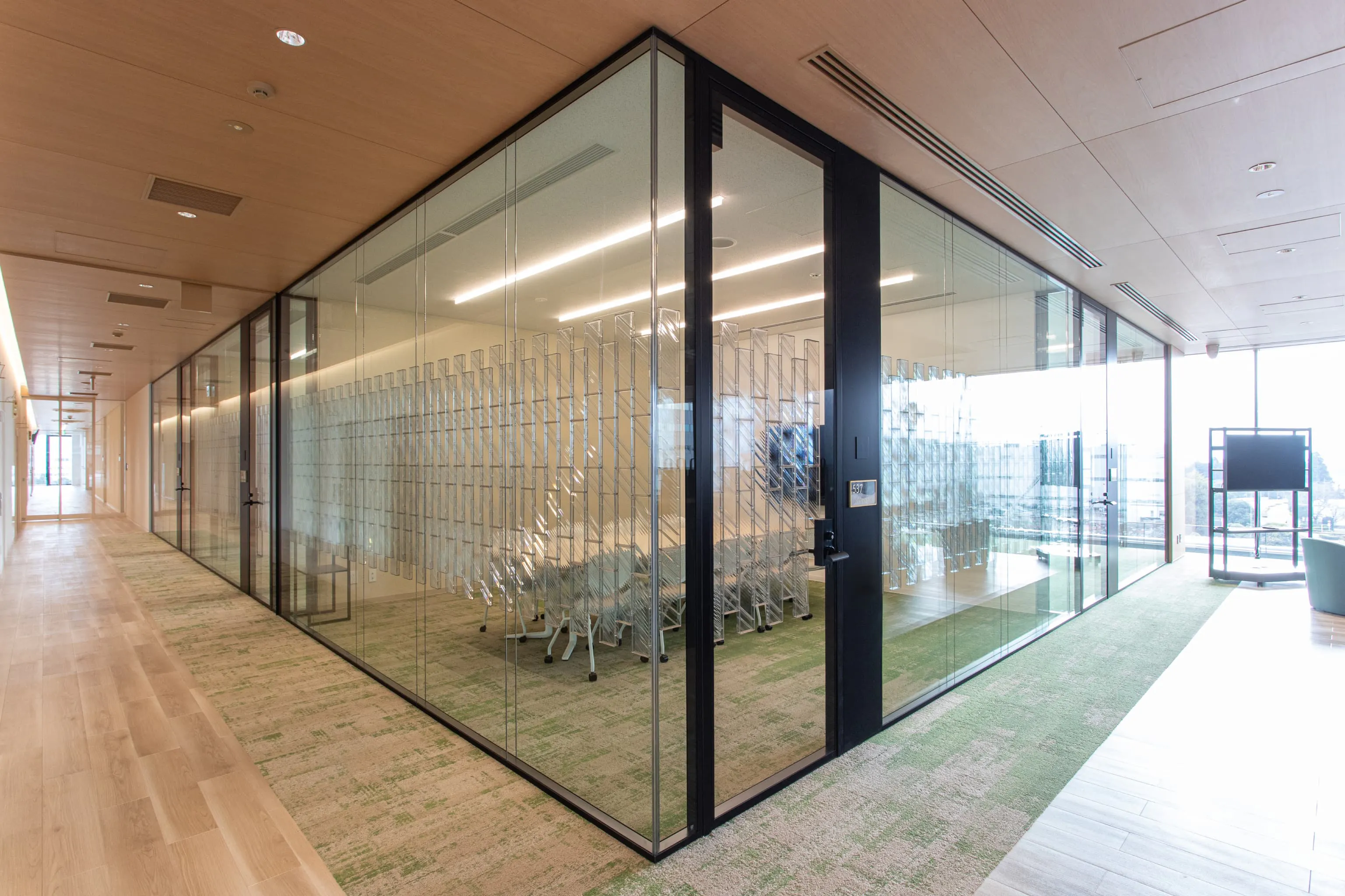 東京エレクトロン九州株式会社 様の事例写真／[3F会議室]KYOSOエリアに隣接する、ガラスの壁に囲まれた会議室。開放感はありつつも、透明な吸音パネルが音漏れ防止と、さりげない目隠しの役割を果たしています。来客との打ち合わせから社内会議まで幅広く使える場です。