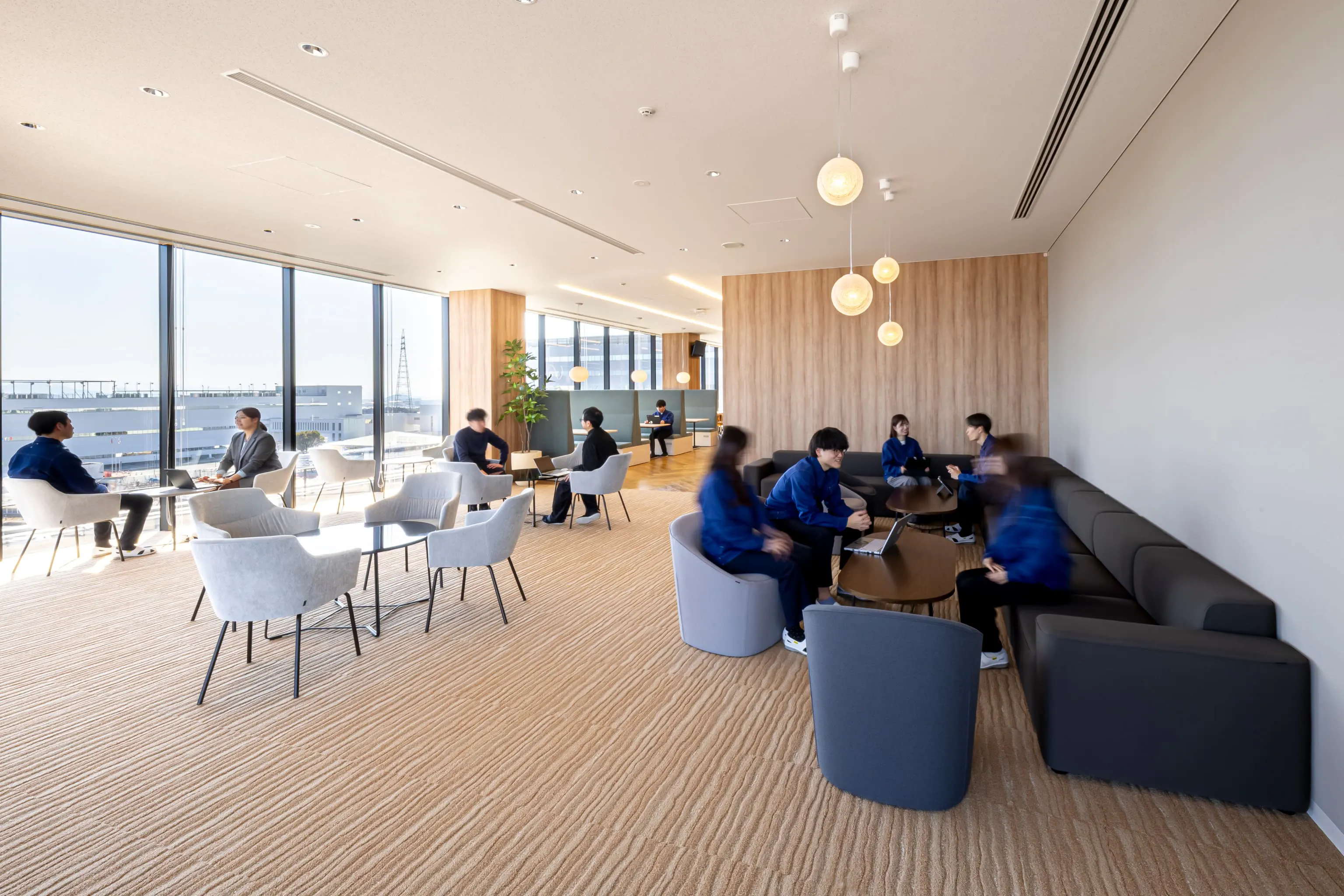 東京エレクトロン九州株式会社 様の事例写真／[4F休憩エリア]休憩エリアの奥へ進むと、カーペット敷きの落ち着いた空間が広がります。ホテルのラウンジを思わせるシックな家具が配置され、窓際のソファ席からは阿蘇の山並みを一望。より静かに休息できる場となっています。