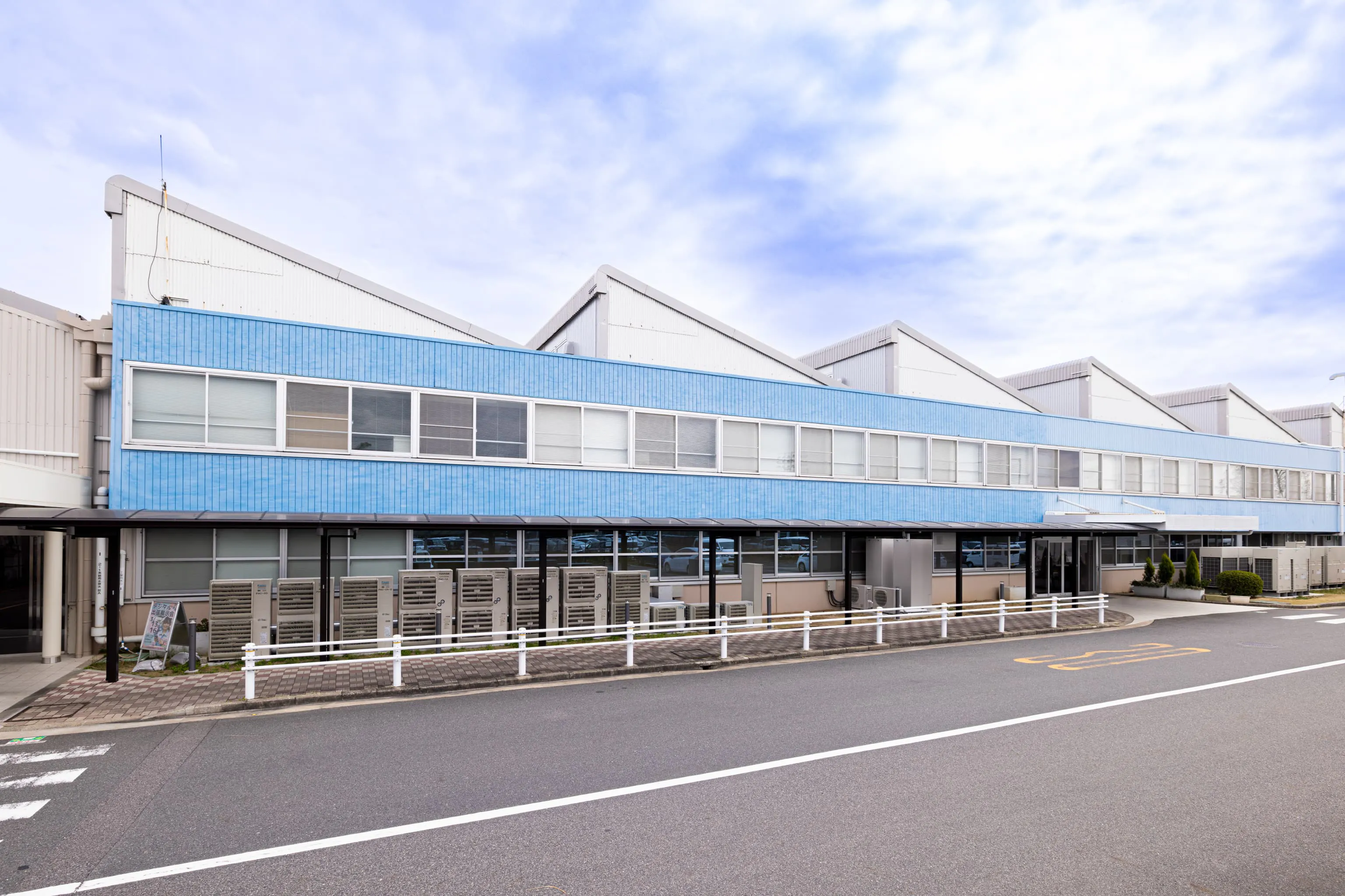 株式会社デンソー安城製作所 様の事例写真／[外観]ノコギリ屋根が特徴的で、自然光がほどよく入るように天窓は北側に設置されています。壁は清潔でクリーンな印象のブルーを取り入れた外観です。