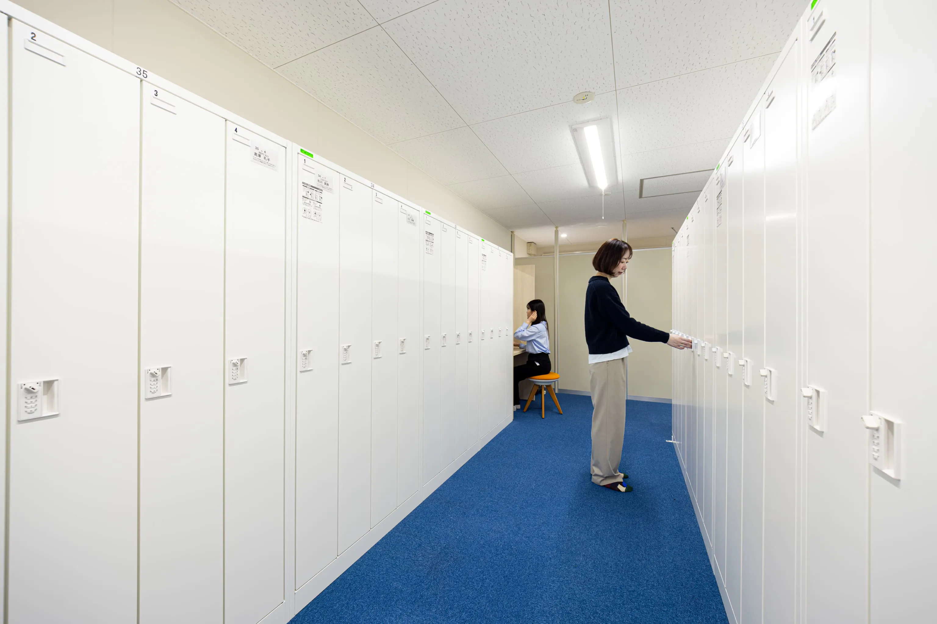 株式会社デンソー安城製作所 様の事例写真／[1Fロッカールーム（女性用）]従業員用エントランスの横には、ロッカールームがあります。青い絨毯が敷き詰められた清潔感のあるデザインです。シャワー室やドレッサーも完備されています。