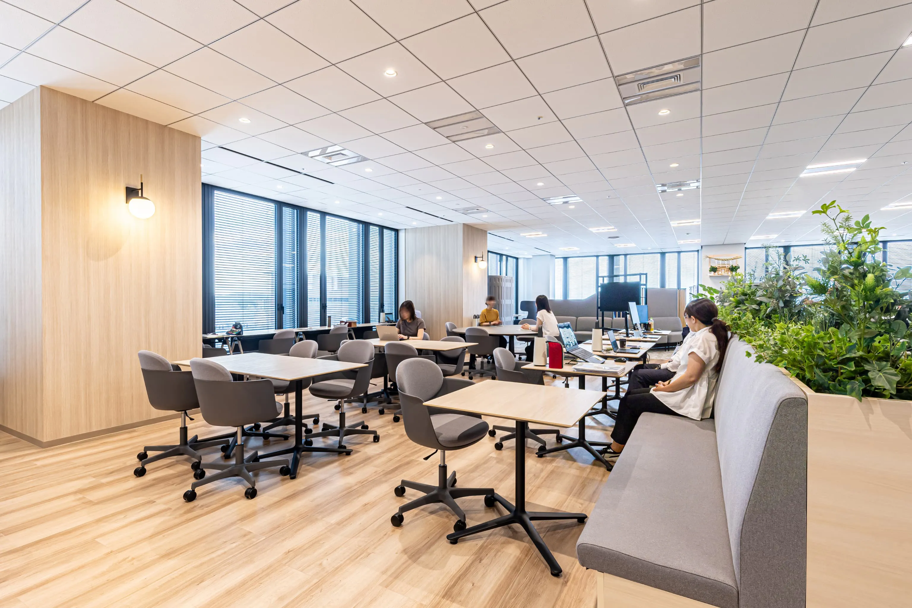 西鉄エアサービス株式会社 様の事例写真／[カフェ＆ワークスペース]暖色の照明が採用され、仕事モードから気持ちを切り替えてリラックスできる空間となっています。カフェスペースの居心地の良さをそのままに、肩の力を抜いて作業に臨めるワーキングエリアです。
