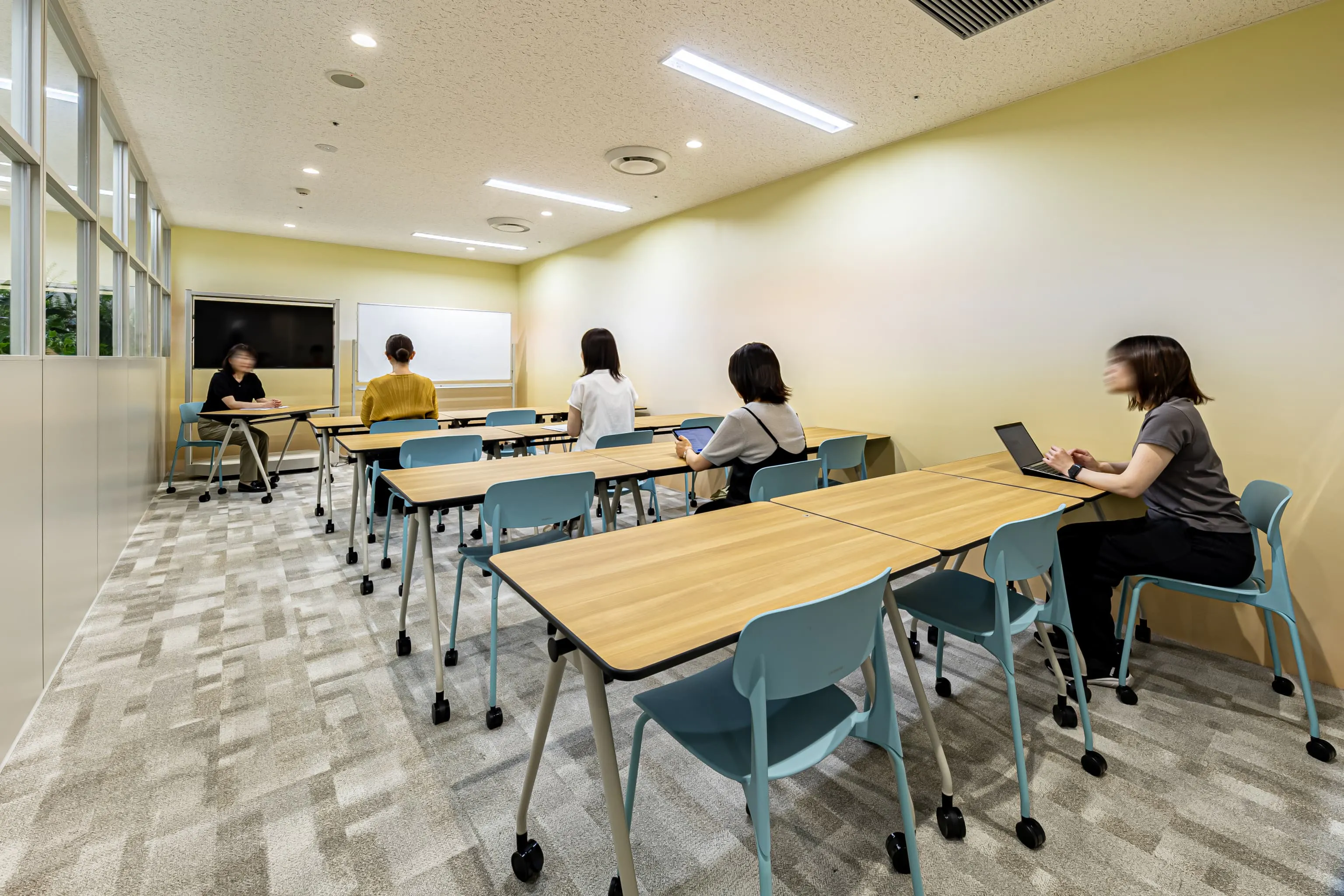 西鉄エアサービス株式会社 様の事例写真／[会議室]研修や教育、社内ミーティングなど多目的に活用される会議室です。閉塞感を和らげるため、壁面には陽だまりのような温かみのある壁紙を採用。間仕切りの一部をガラスにすることで、圧迫感が巧みに軽減されています。