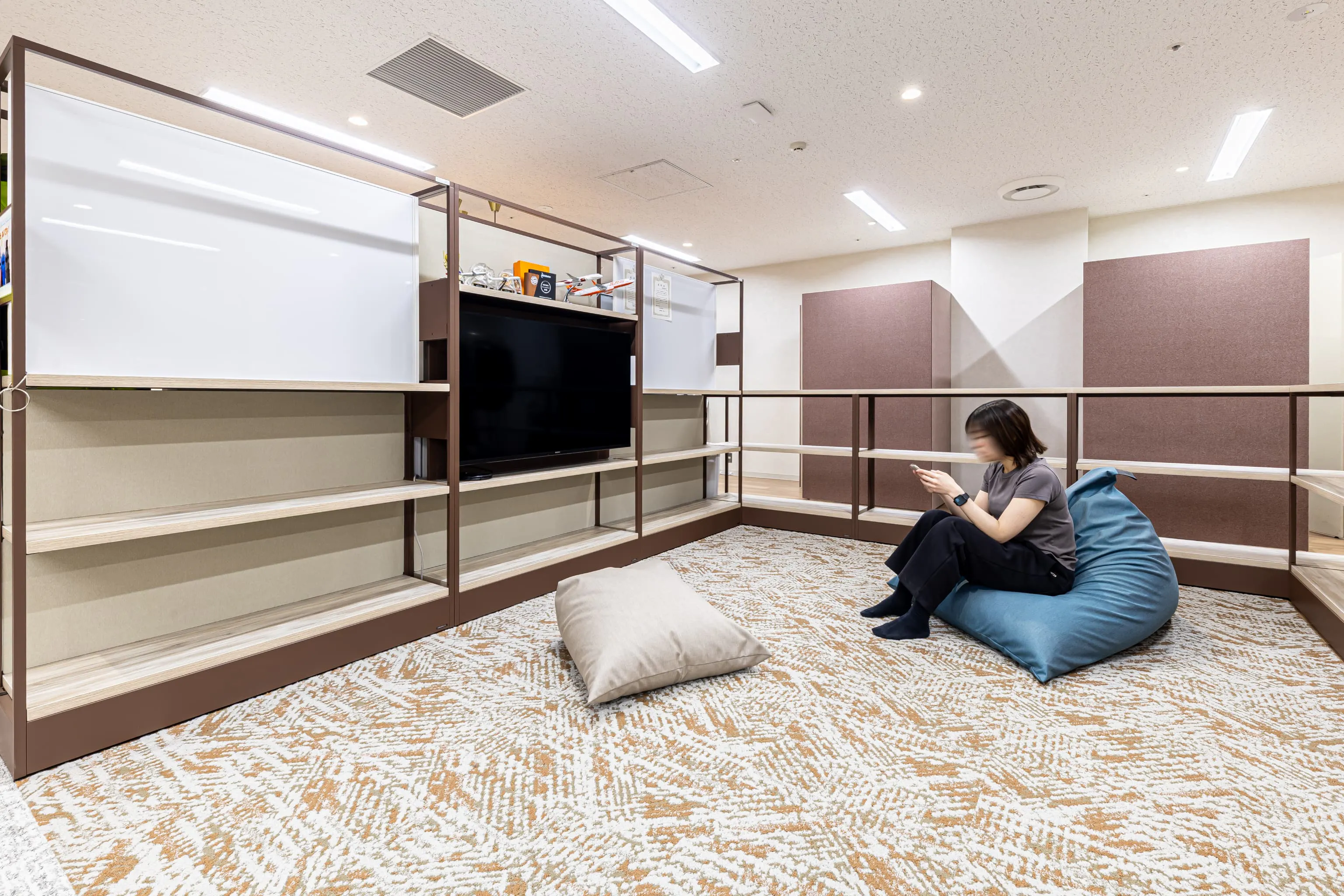 西鉄エアサービス株式会社 様の事例写真／[みんなのリビング]「夏休みや子どもの体調不良など、いざという時は子連れでの出社にも対応できるように」と用意されたカーペット敷のリビングスペースです。働く子育て世代に寄り添う設計には、「社員ファースト」の精神が表れています。