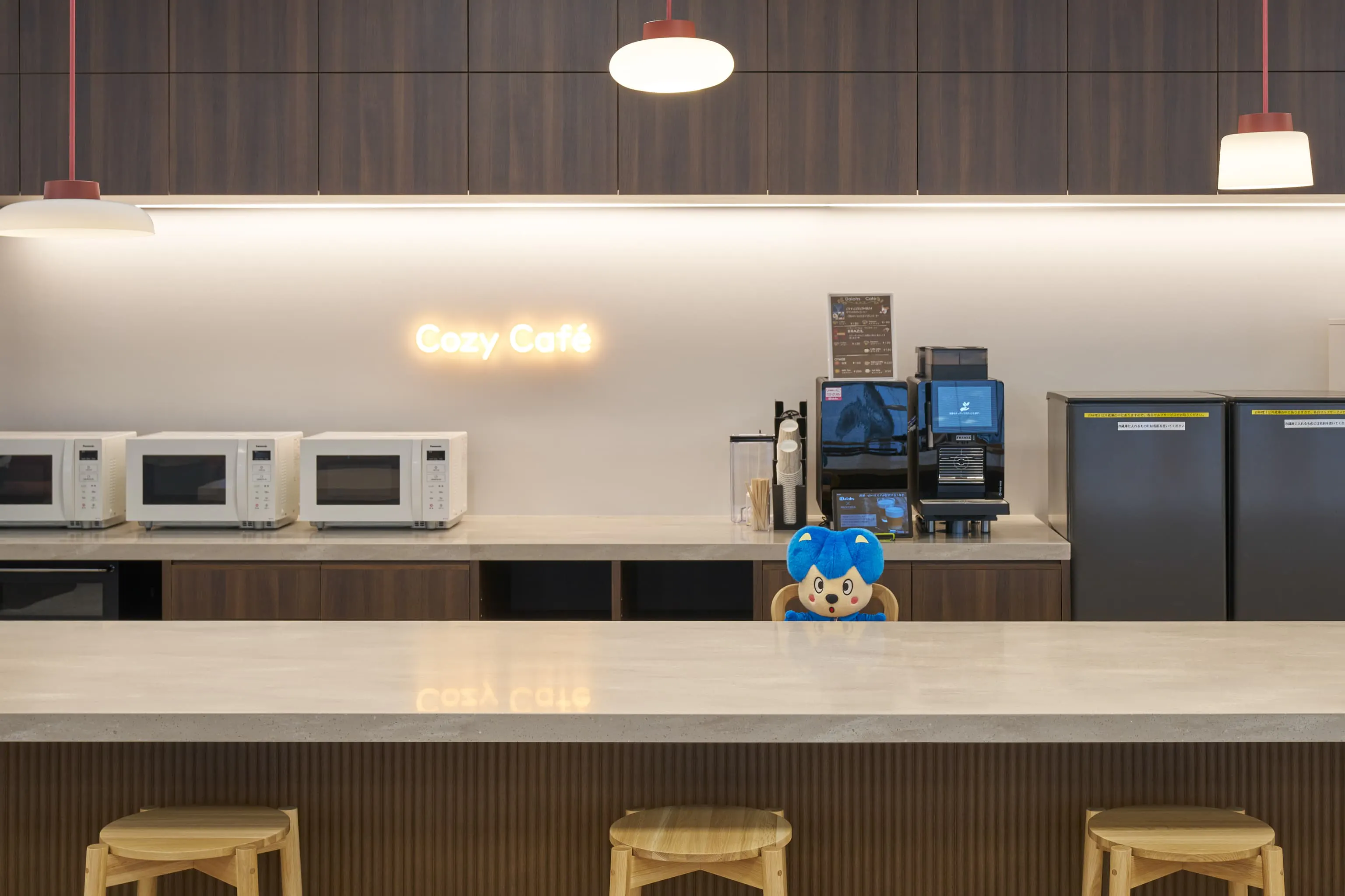 三菱電機エンジニアリング株式会社 様の事例写真／[10FCozy Café]こだわりのコーヒーを淹れられるカフェカウンター。電子レンジや冷蔵庫も備え、気軽な会話が生まれやすいスポットです。自社キャラクター「エンジくん」がお店番をしているようにちょこんと置かれ、訪れる人を和ませています。