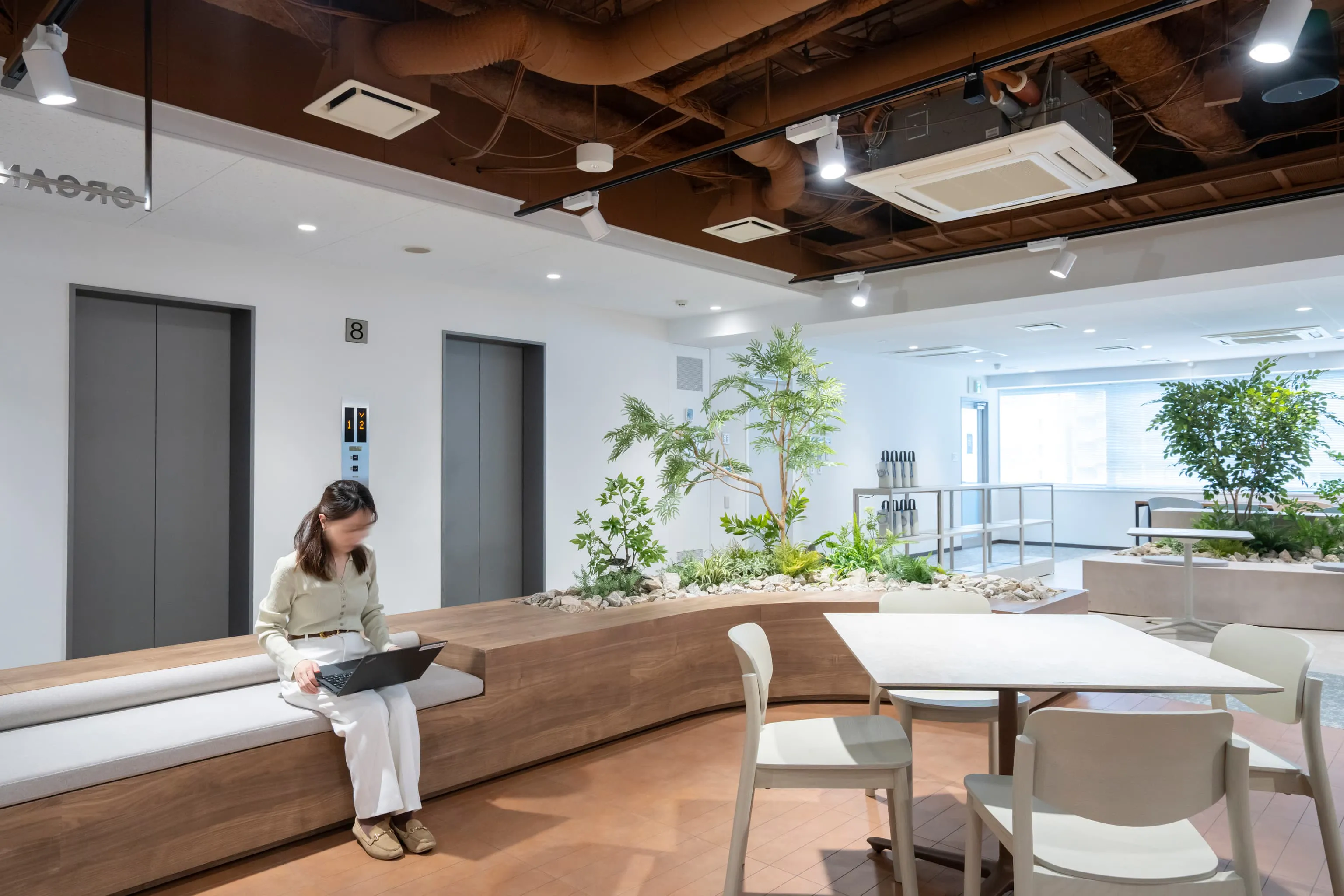 オルガノ株式会社 様の事例写真／[8Fフリーエリア]木目柄ベンチに大きな木を植え込み、社内ながらまるで屋外の都市公園に来たかのような雰囲気です。一人で休憩をしたり、複数人でお弁当を広げてランチをしたり、ビル全体の人々が集まり自然と交流が生まれています。